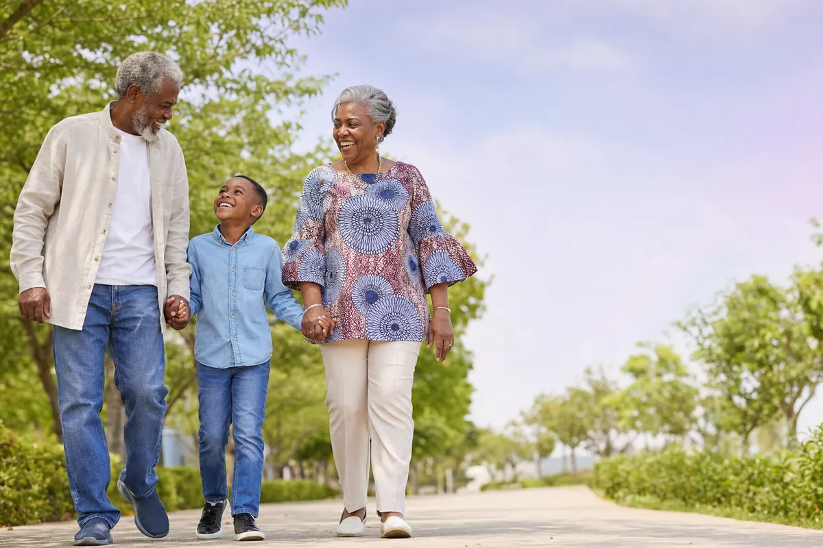 Nigerian grandparents walking hand in hand with grandson along a sunny park path