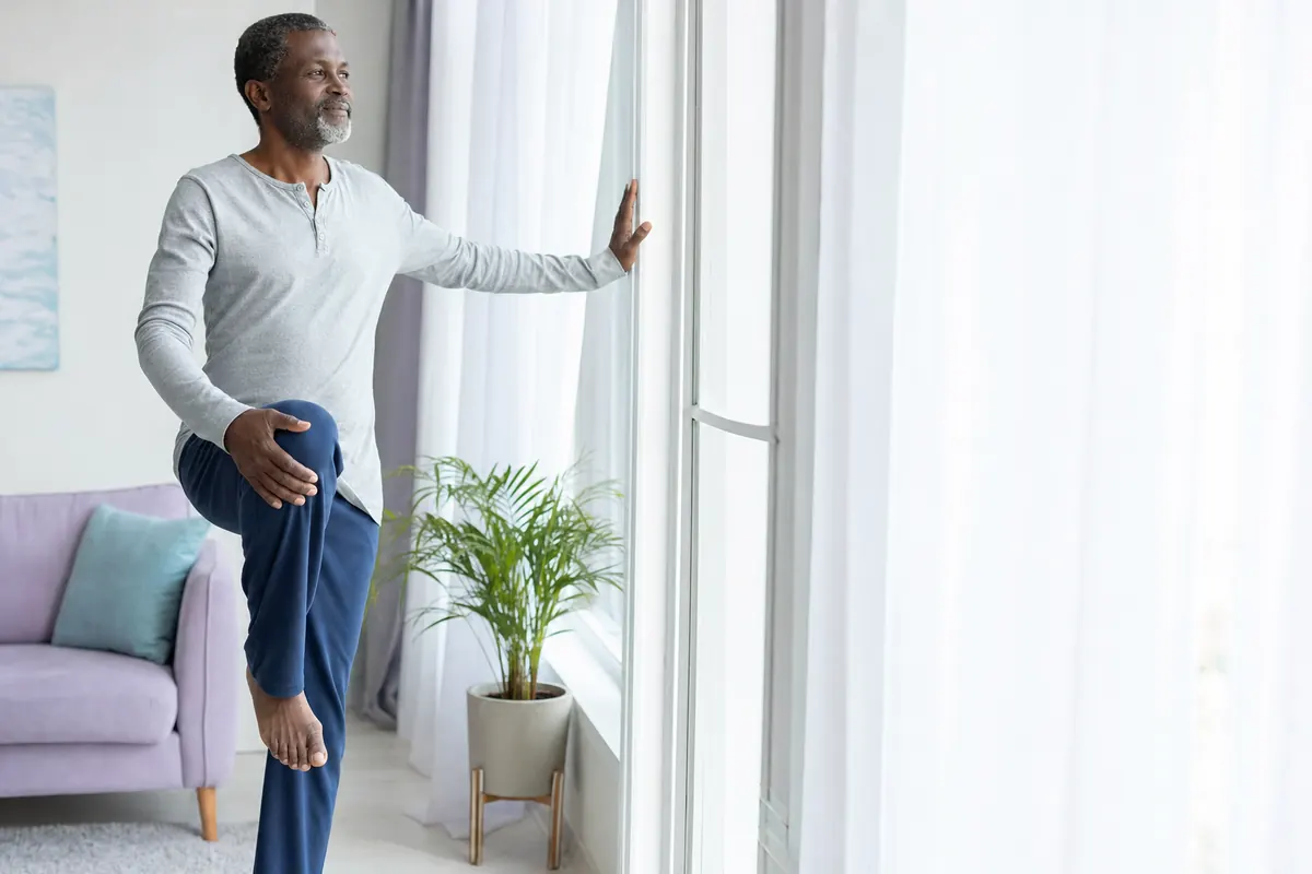 Nigerian man in his fifties gently stretching his leg by a bright window